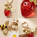 A charming keychain with a red strawberry, a bumblebee and a daisy charm on a golden heart clasp